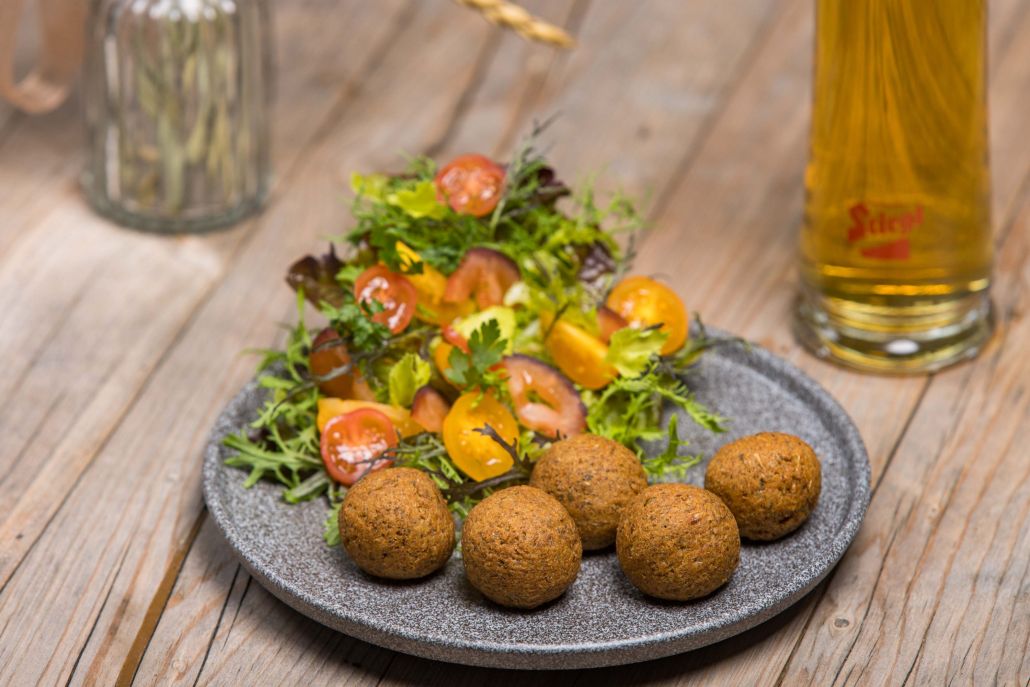 Ein Teller mit Salat und veganen Bällchen, dazu ein Bier